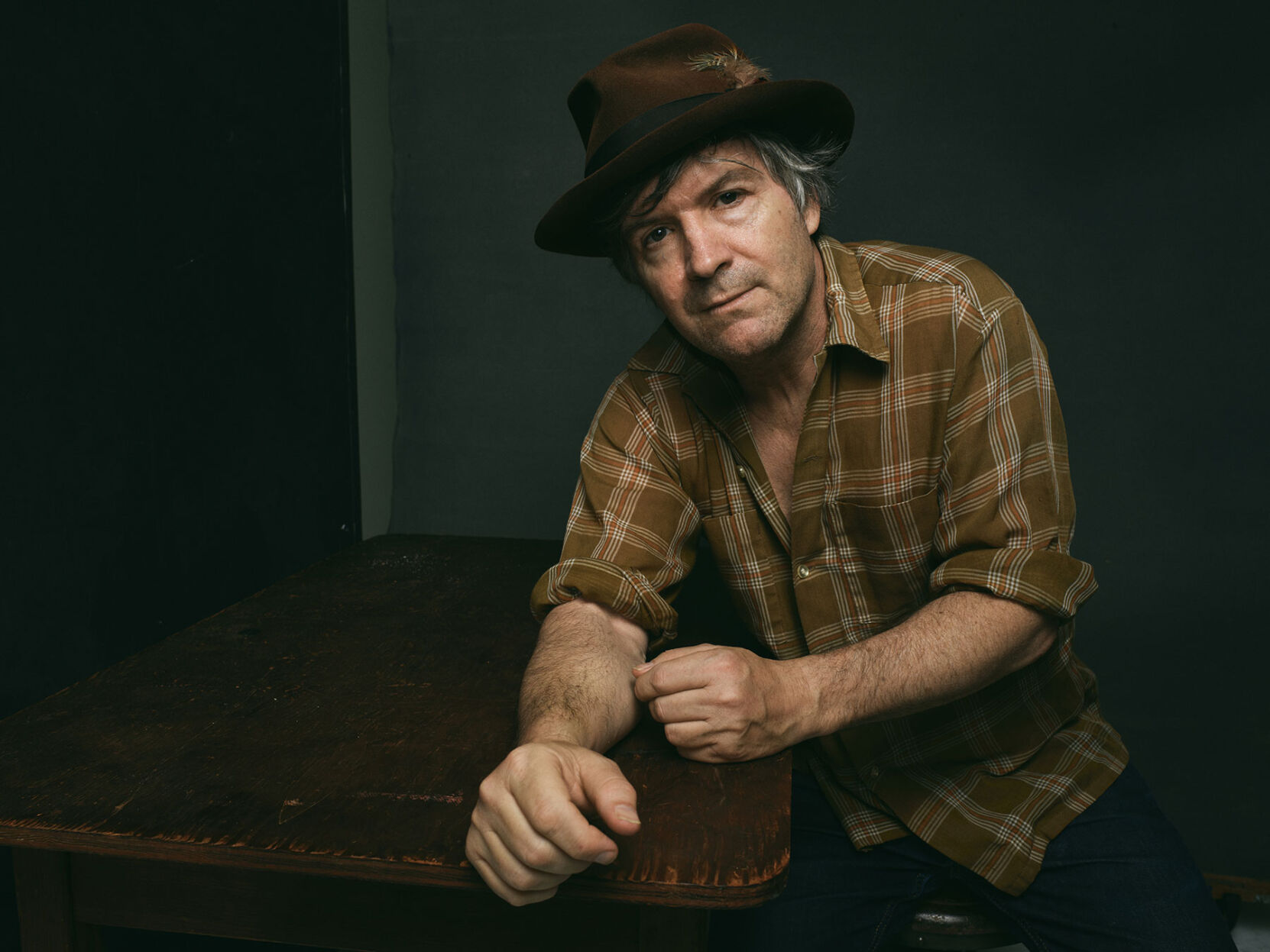 Tim Easton press photo artist poses in brown flannel shirt against gray background